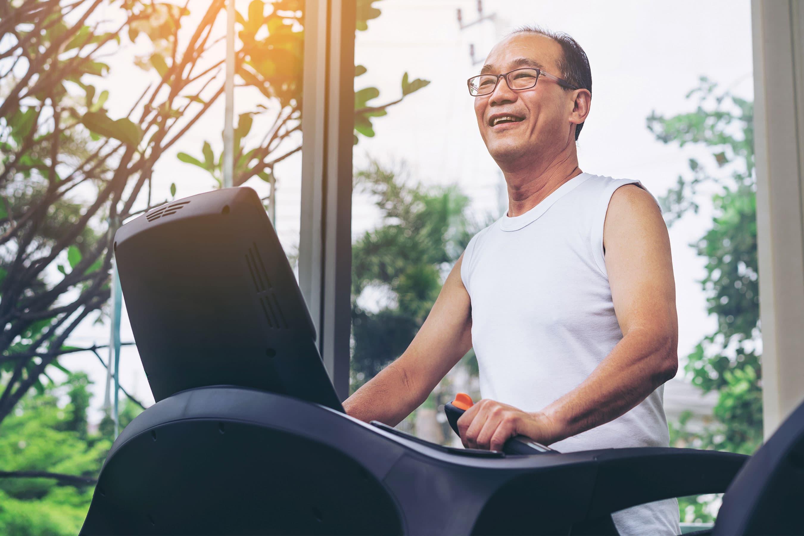 A man smiling while walking on a treadmill in a brightly lit gym.