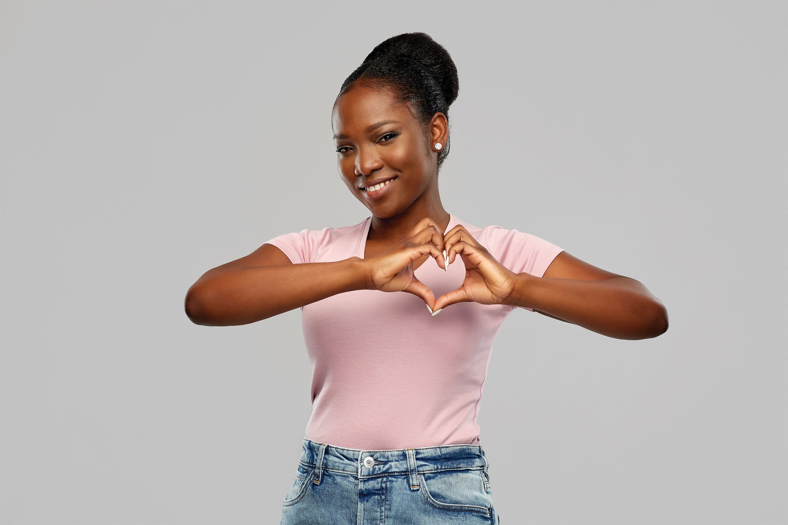 A smiling woman forming a heart shape over her chest with her hands.