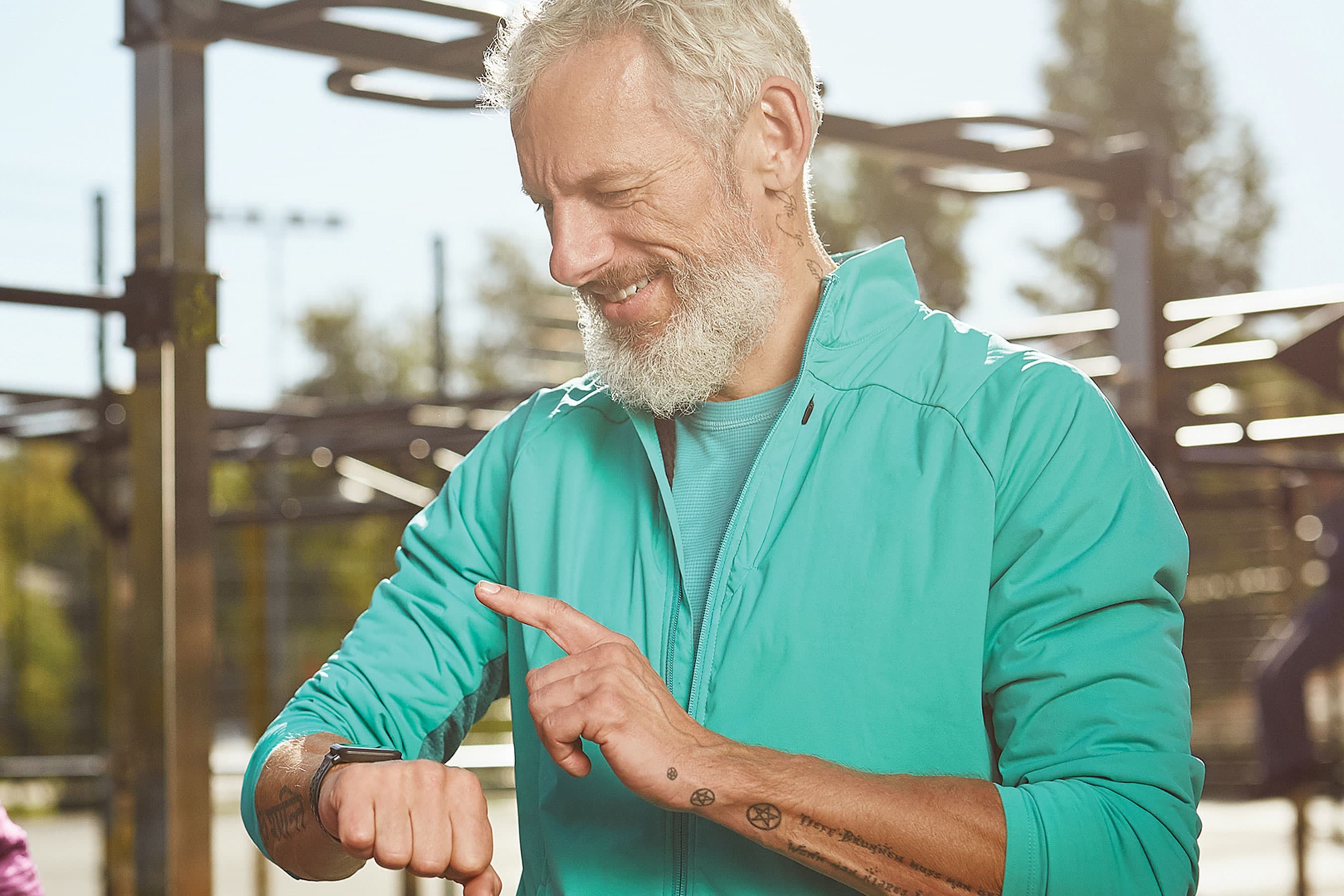 An older man smiling while looking down at a smartwatch on his wrist outdoors.
