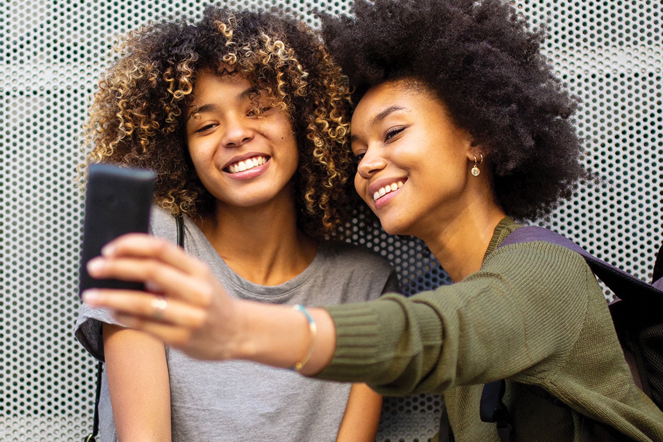 Two people smiling together while looking at a smartphone held up for a selfie.