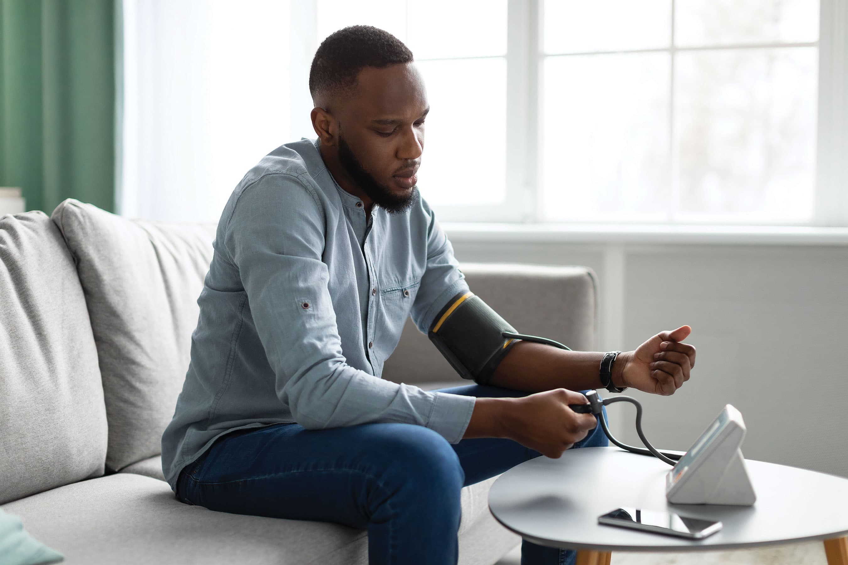 A person sitting on a sofa and using a digital blood pressure monitor on their arm.