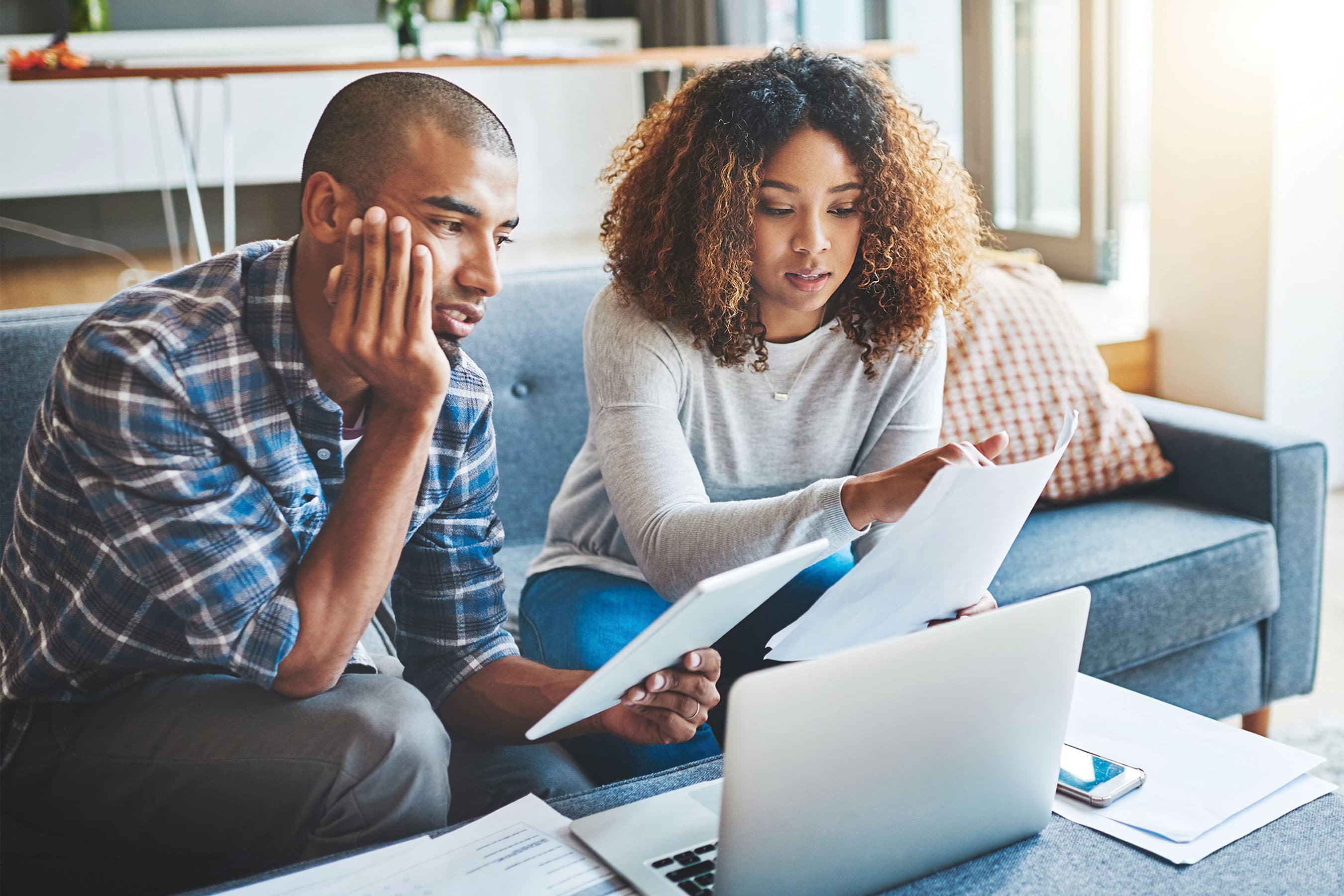 Two people seated together looking at paperwork and a laptop screen.