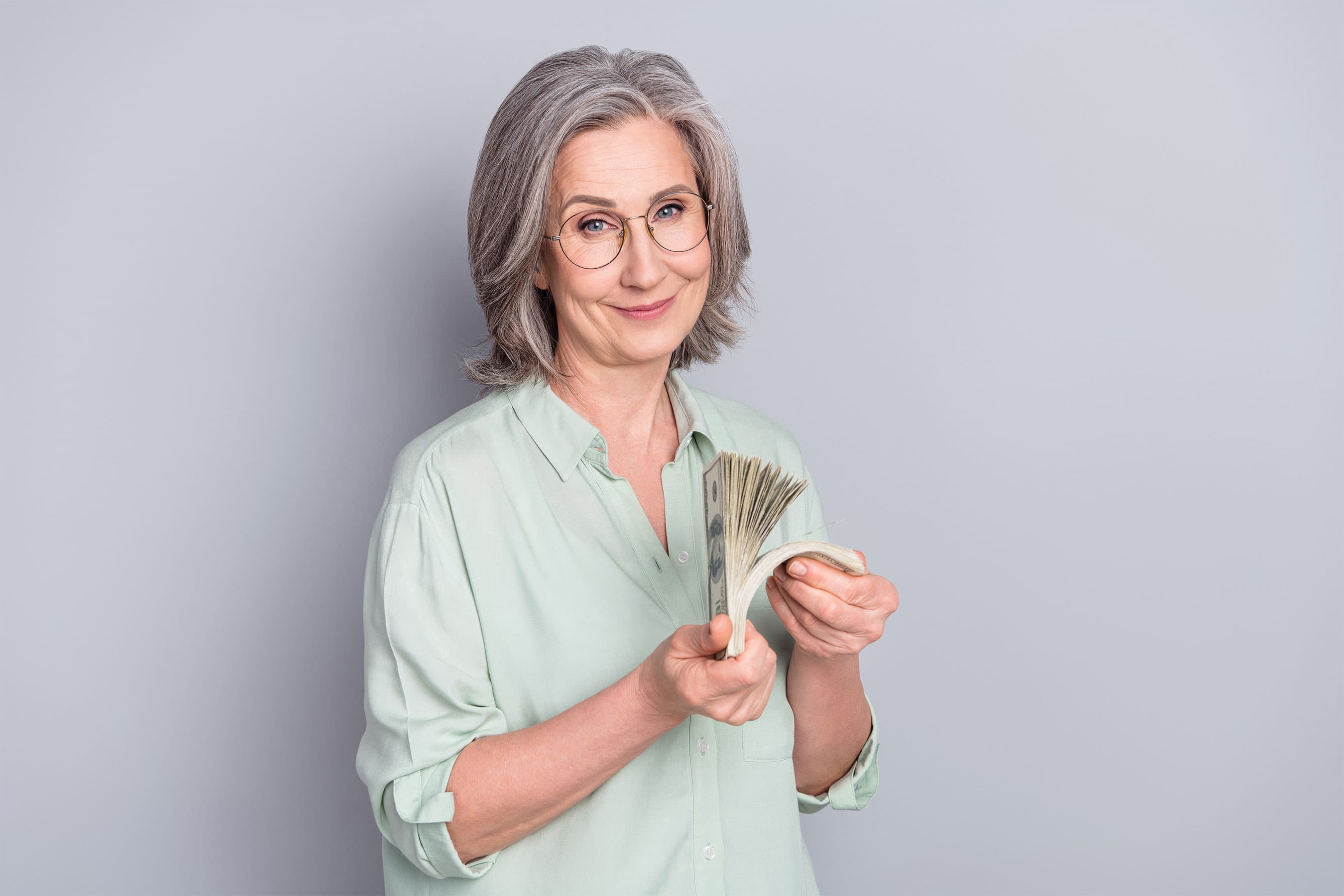 A woman standing against a plain background holding cash in her hands.