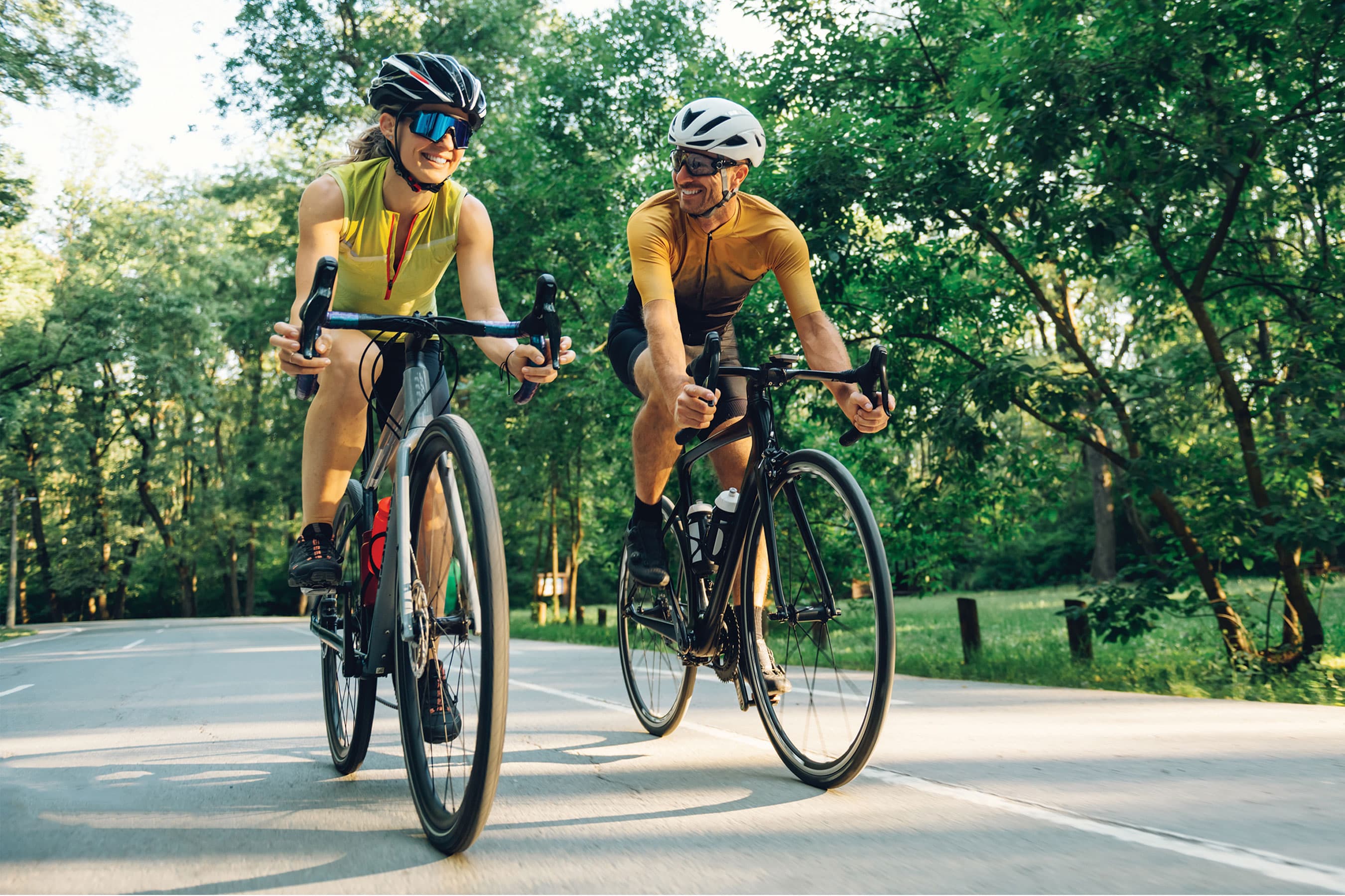 Two cyclists riding bicycles on a paved road surrounded by trees.